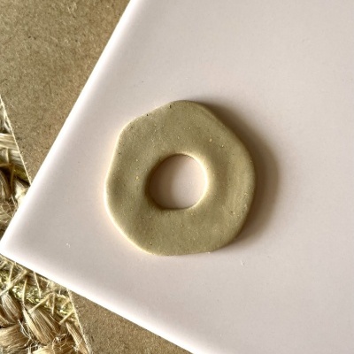 Peça circular bege claro com orifício central sobre superfície rosa clara