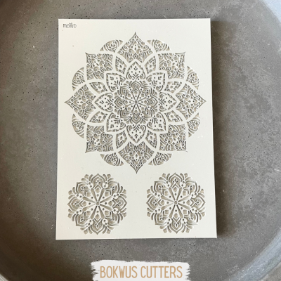 Folha com moldes recortados de mandalas em branco sobre superfície cinza