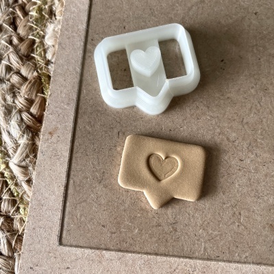 Cortador de biscoitos branco em forma de balão de diálogo com coração e massa cortada similar sobre superfície de madeira.