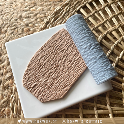 Peça de massa castanha texturizada e rolo azul claro sobre placa branca e superfície de fibras naturais