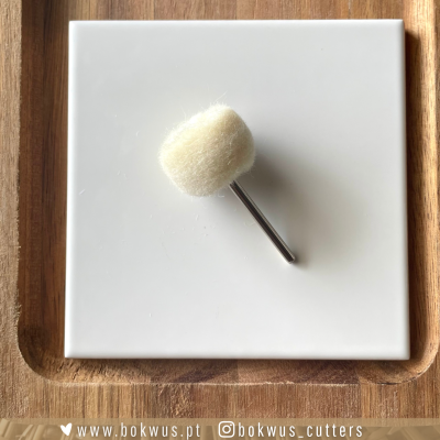 Almofada polidora de feltro branco com eixo metálico sobre azulejo branco e tabuleiro de madeira clara