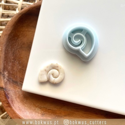 Cortador de biscoitos em forma de concha e biscoito espiral sobre base branca e madeira