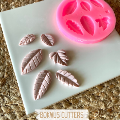 Molde de silicone rosa com formas de folhas e peças cortadas em tons de rosa claro sobre suporte branco.