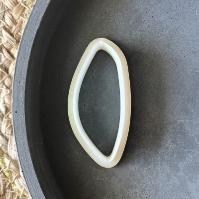 Pulseira rígida branca oval irregular em tigela preta, sobre tapete de fibras naturais