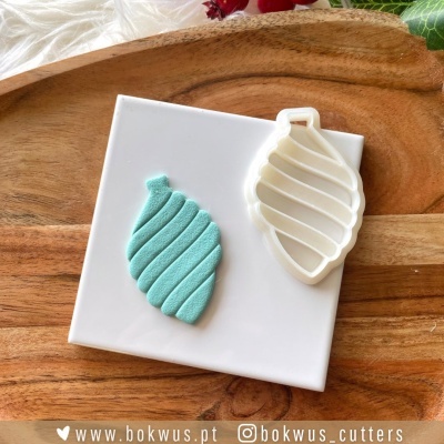 Cortador plástico branco em forma de folha e pasta fondant verde aguarela com textura em espiral sobre base branca e tábua de madeira