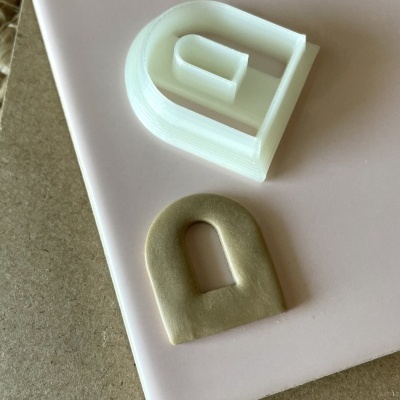 Dois objetos arqueados, um plástico branco e um de cerâmica bege, sobre superfícies rosa e castanha