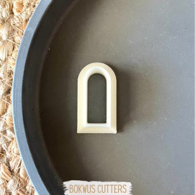 Cortador de biscoitos branco em prato preto sobre superfície de juta com etiqueta BOKWUS CUTTERS