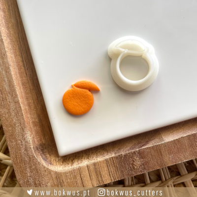 Corte em feltro laranja e peça plástica branca sobre superfície branca e tabuleiro de madeira