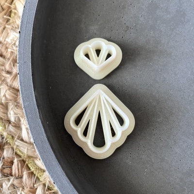 Dois objetos brancos em forma de concha com padrão geométrico em superfície cinza e tecido natural.