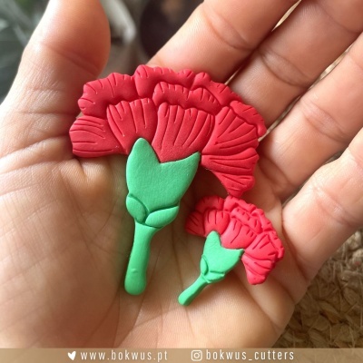 Duas peças vermelhas com talos verdes em formato de cravos na mão