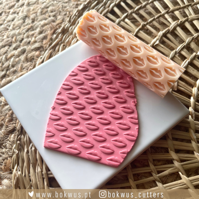 Rolo de textura para pasta com padrão de lábios e pasta rosa com mesma textura sobre placa branca