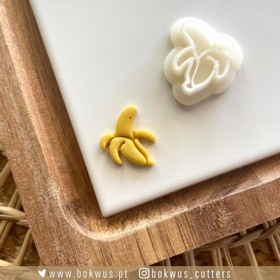 Cortador de biscoitos em forma de banana e biscoito amarelo no descanso de madeira.