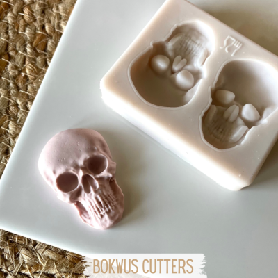 Molde de silicone branco com cavidades em forma de caveira e peça rosa moldada