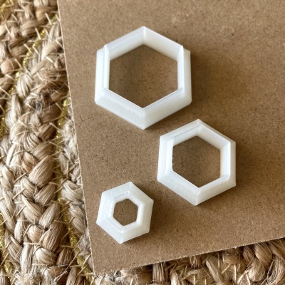 Formas hexagonais brancas em plástico sobre papel castanho com fundo de tecido trançado bege