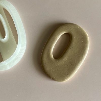 Molde branco plástico e peça de massa oval com buraco no meio sobre superfície rosa clara