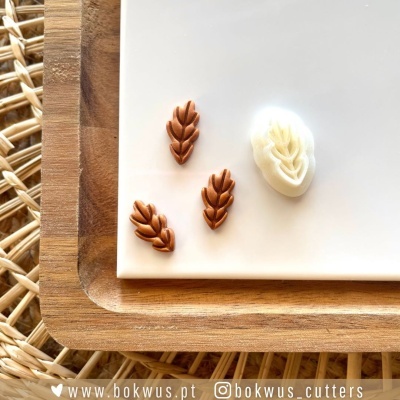 Moldes em formato de espiga de trigo castanhos e branco numa bandeja branca sobre base de madeira e tapete de palha