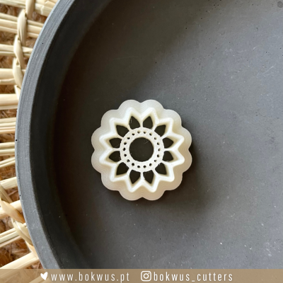 cortador de biscoitos em formato de flor branco sobre superfície cinza