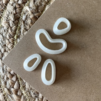 Quatro anéis decorativos brancos com formas orgânicas sobre superfície castanha