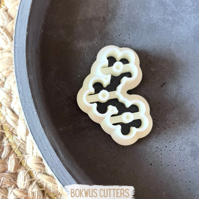 Cortador plástico branco com 3 buracos circulares sobre prato escuro com tapete de fibra e etiqueta BOKWUS CUTTERS