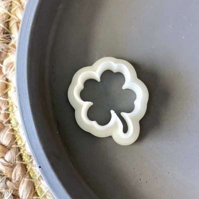 Cortador de bolachas branco em forma de folha dentro de prato cinzento sobre superfície de fibra trançada