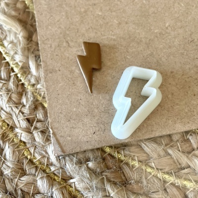 Cortador de bolachas branco em forma de raio e bolacha castanha cortada na mesma forma sobre cartão e fundo tecido