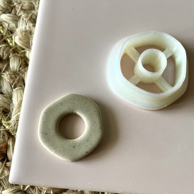 Dois objetos circulares, cerâmica bege e plástico branco, sobre superfície rosa