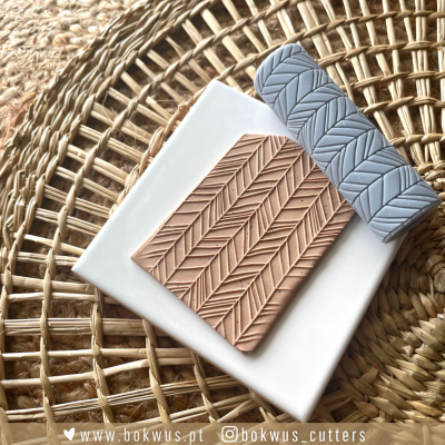 Rolo de silicone azul com padrão e massa com relevo do mesmo padrão sobre placa branca, sobre tapete de palha trançada