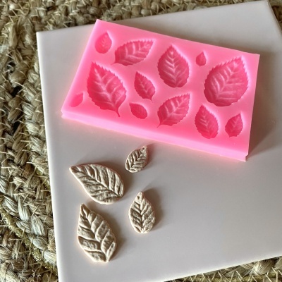 Molde de silicone rosa com cavidades em forma de folhas e folhas brancas feitas à frente sobre superfície branca