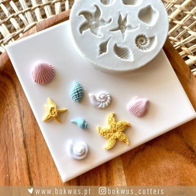 Molde de silicone branco com conchas e estrelas do mar e objetos coloridos em placa branca sobre base de madeira