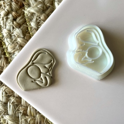 Carimbo branco com desenho abstrato e uma impressão em argila cinzenta, sobre superfície cor de rosa e tapete têxtil bege