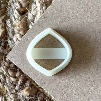 Acessório de plástico branco em formato losango sobre madeira clara e tapete de fibras naturais