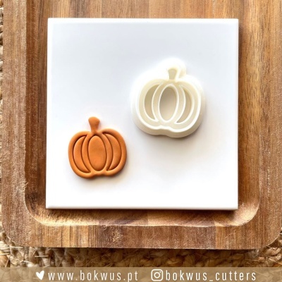 Cortadores de biscoitos em forma de abóbora, branco e castanho claro, sobre placa branca e tábua de madeira