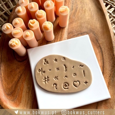 Carimbos de silicone de símbolos variados sobre base branca, velas cor de pêssego numa superfície de madeira