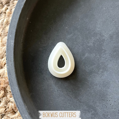 Cortador em forma de gota branco sobre prato preto e tapete de fibras