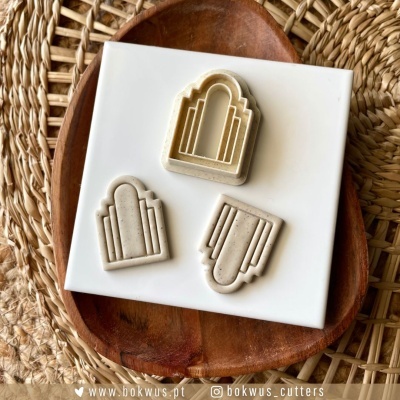 Três cortadores de biscoitos geométricos sobre placa branca e prato de madeira em esteira de palha