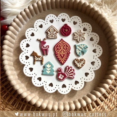 Moldes decorativos em plástico colorido para bolachas com formas natalícias sobre um prato branco com padrão de corações.