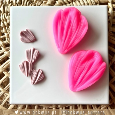 Moldes de silicone rosa em forma de pétalas sobre suporte branco com fundo de tecido trançado