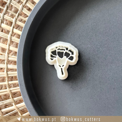 Cortador de massa branco em forma de flor sobre prato cinzento e fundo de palhinha