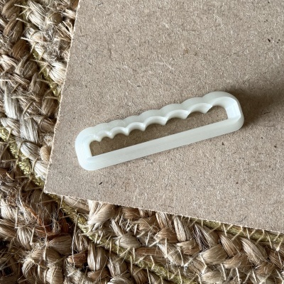 Cortador de plástico branco com bordas onduladas sobre madeira e tapete de fibras naturais.