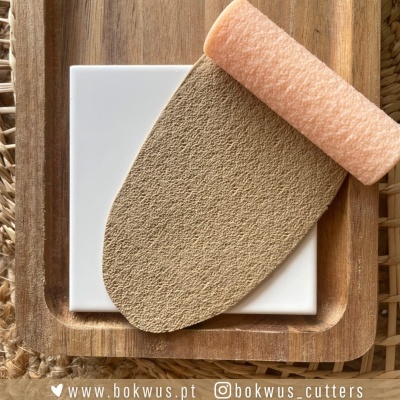 Placa branca quadrada com rolo de espuma cor de pêssego e folha texturizada castanha sobre tábua de madeira