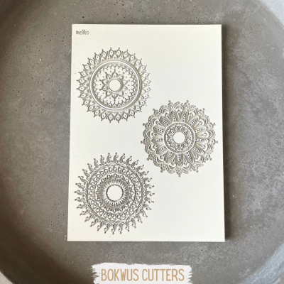 placa branca com três mandalas cinzentas decorativas sobre superfície cinza