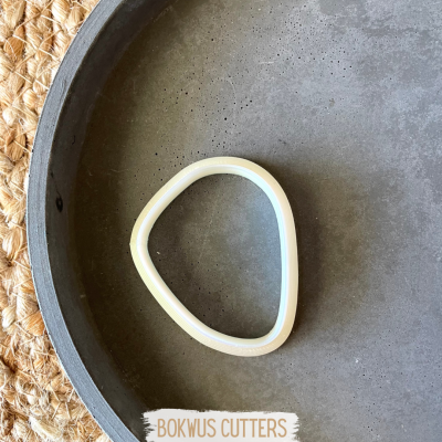 Cortador ou anel de silicone branco num prato cinza sobre superfície de fibras naturais.