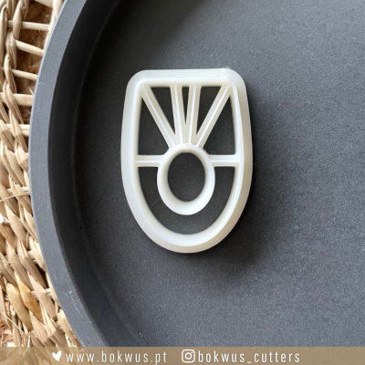 Cortador de biscoitos branco com design geométrico sobre fundo preto e cesto de fibras naturais