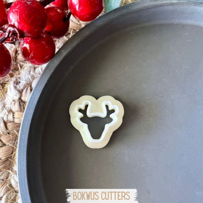 Molde cortador de bolachas branco em forma de cabeça de rena num prato cinzento com bagas vermelhas ao lado