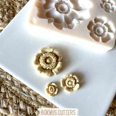 Molde de silicone branco com flores e flores modeladas bege em placa branca sobre superfície de fibra trançada.