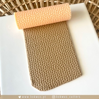 Rolo de textura cor de pêssego com padrão de hexágonos em relevo sobre placa branca