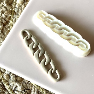 Cortador de biscoitos branco em forma de corrente e biscoito cinzento formato corrente num prato branco