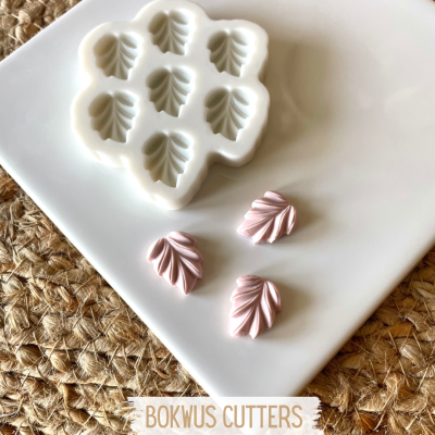 Molde silicone branco com cavidades em forma de folha e três figuras rosas de folha num prato branco