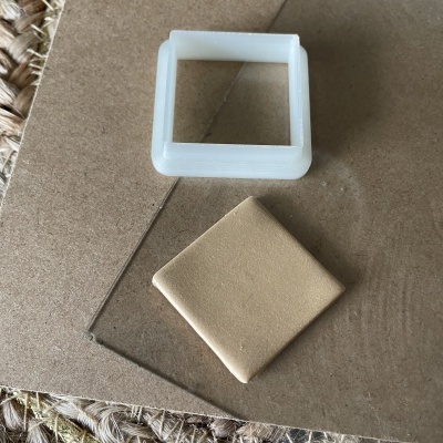 Cortador quadrado branco e peça quadrada de massa bege sobre cartão castanho