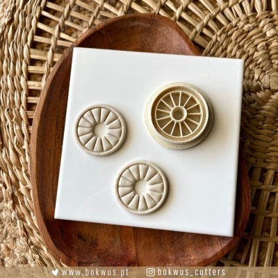 Ferramentas de corte para modelagem de bolo em formato de rodas, sobre prato de madeira e superfície de palha trançada